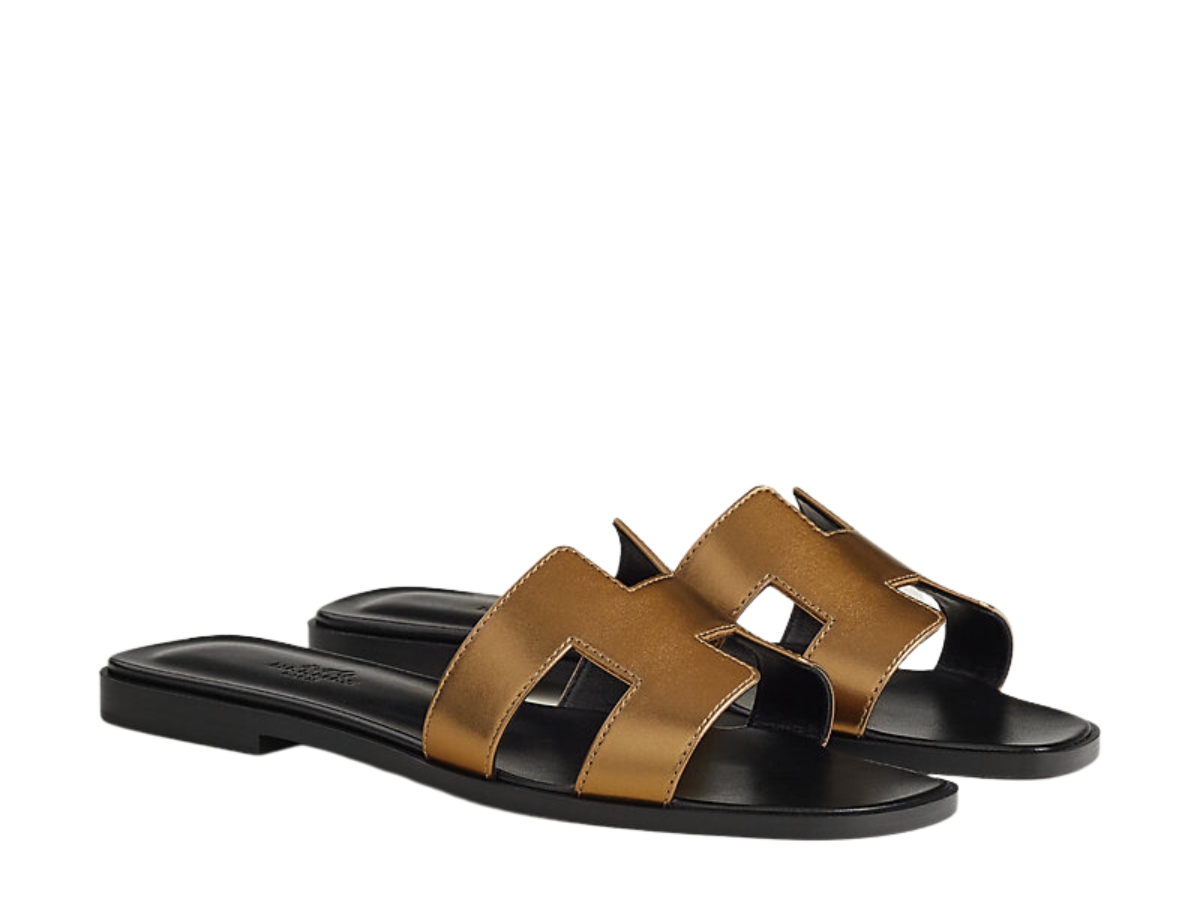 https://d2cva83hdk3bwc.cloudfront.net/hermes-oran-sandal-in-calfskin-with-metallic-finish-and-iconic-h-cut-out-dore-fonce-2.jpg